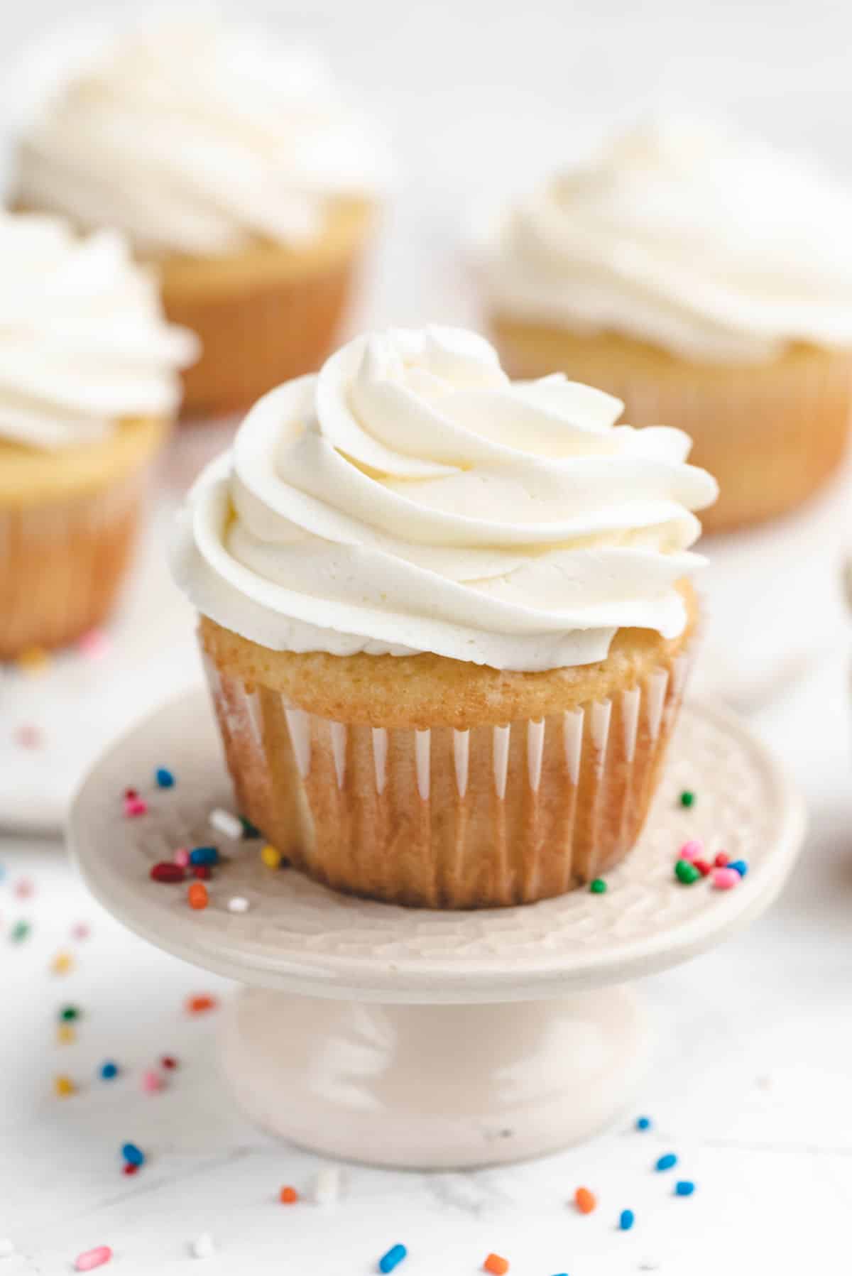A cupcake topped with vanilla buttercream on a cupcake stand. 