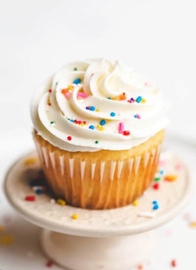 A vanilla cupcake topped with vanilla buttercream frosting and sprinkles.