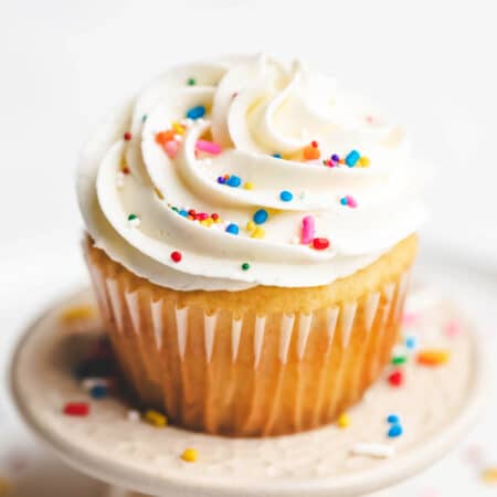 A vanilla cupcake topped with vanilla buttercream frosting and sprinkles.