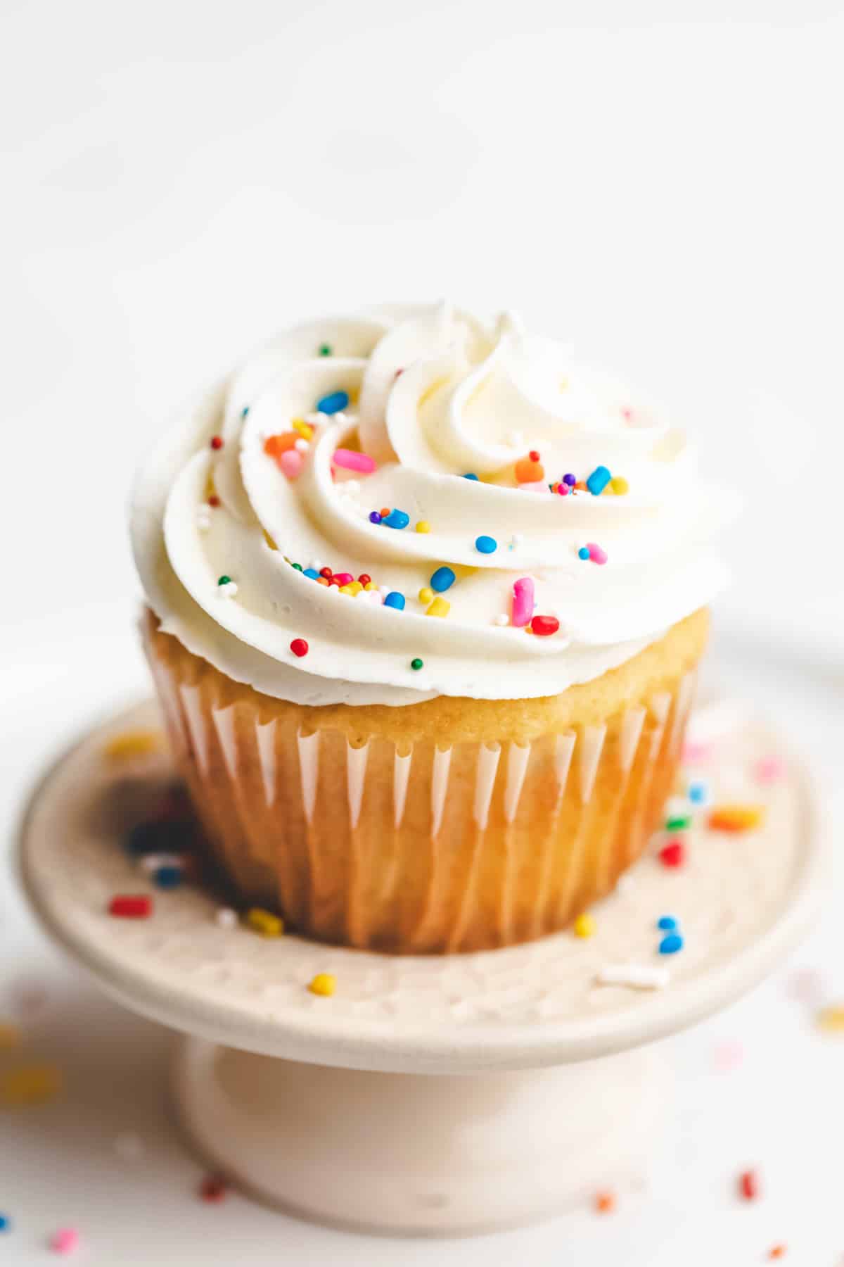 A vanilla cupcake topped with vanilla buttercream frosting and sprinkles. 