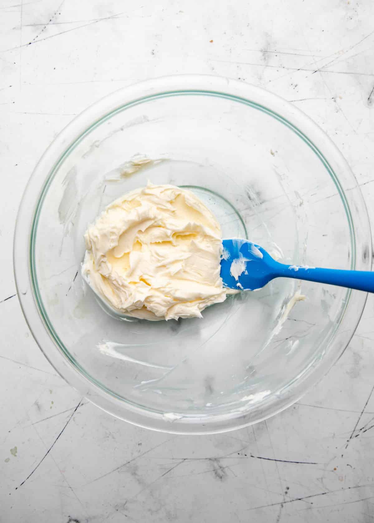 Beaten butter in a glass mixing bowl. 