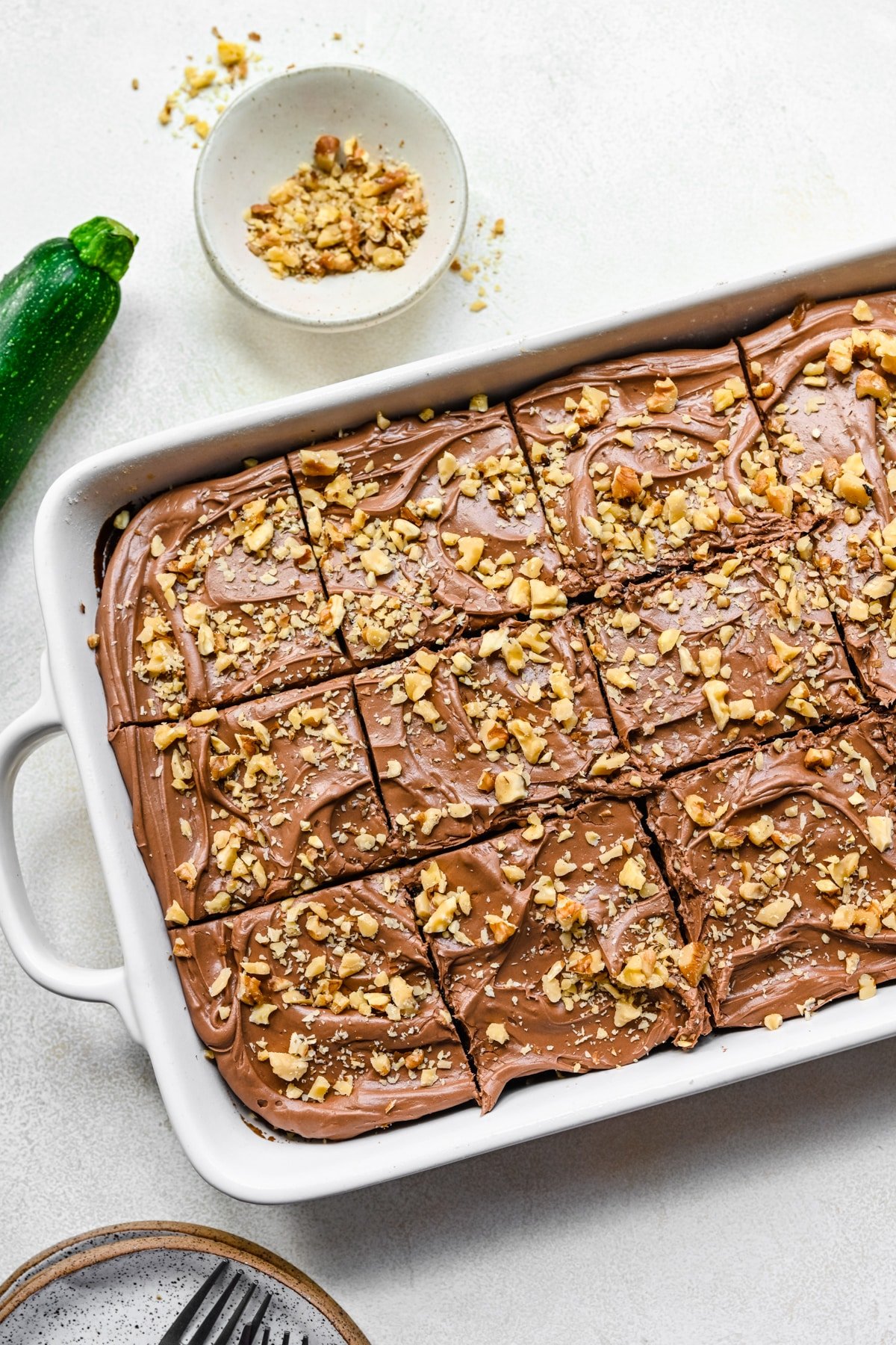Chocolate zucchini cake in topped with chocolate frosting and chopped nuts in a baking pan.