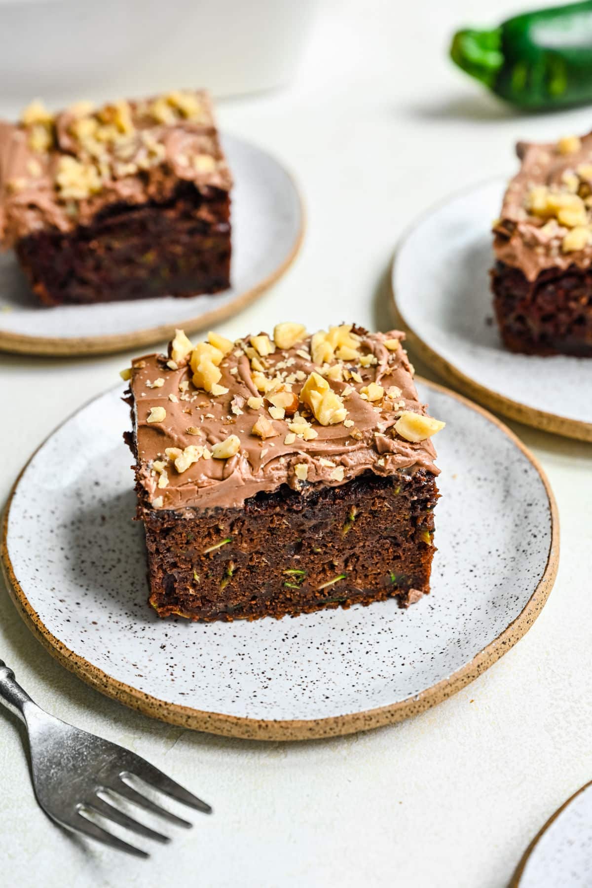 Three slices of chocolate zucchini cake on plates next to a fork.