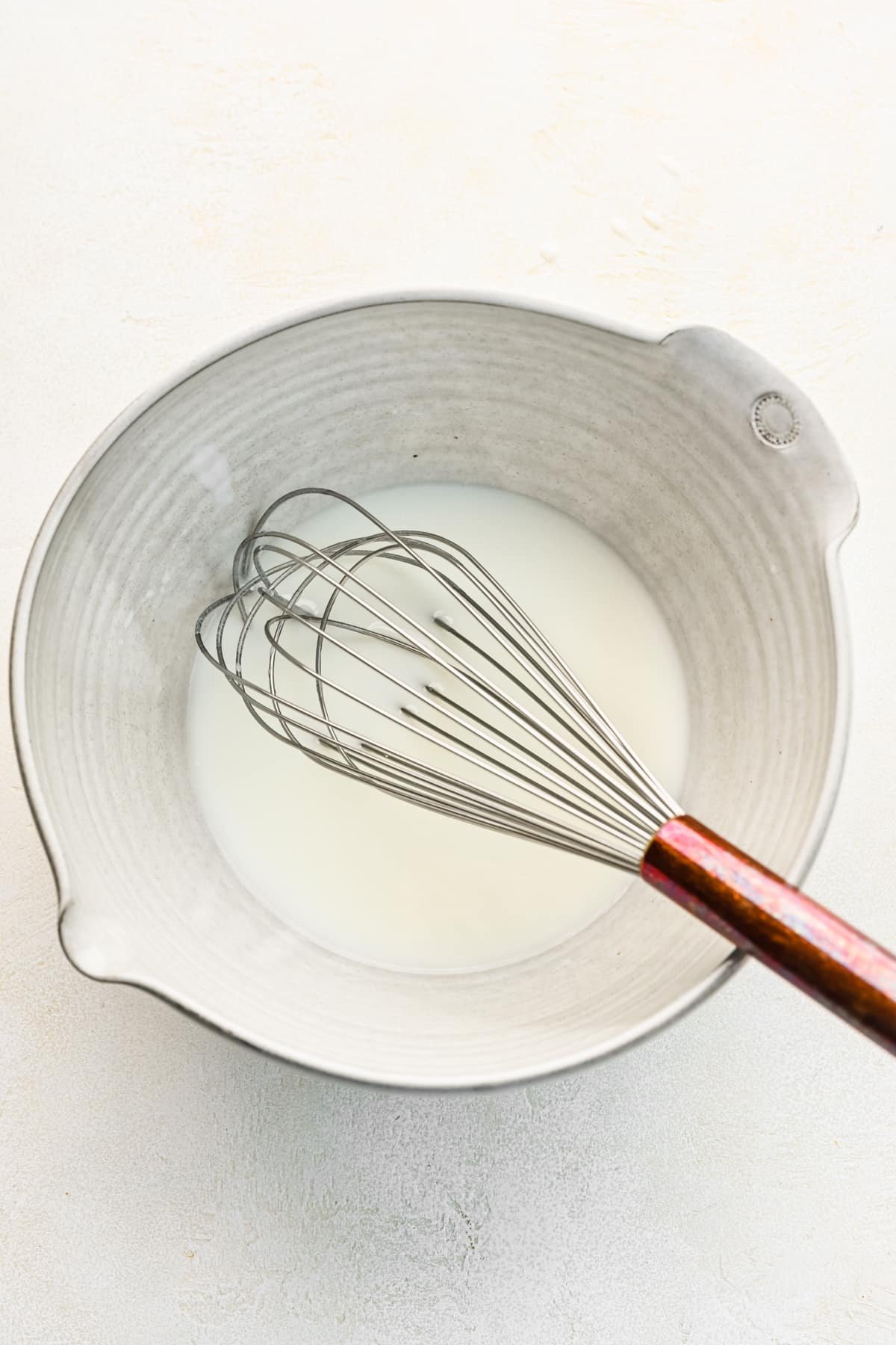 Oil and buttermilk in a mixing bowl with a whisk in it. 