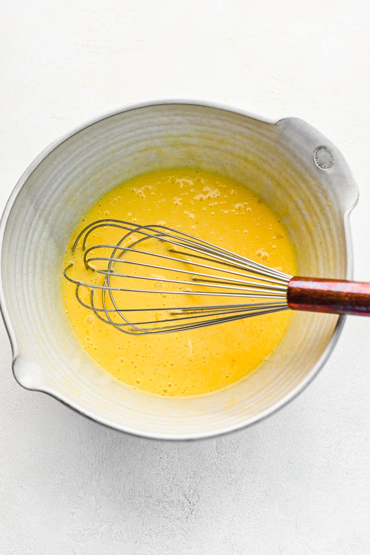 Eggs whisked into oil and buttermilk in a mixing bowl. 