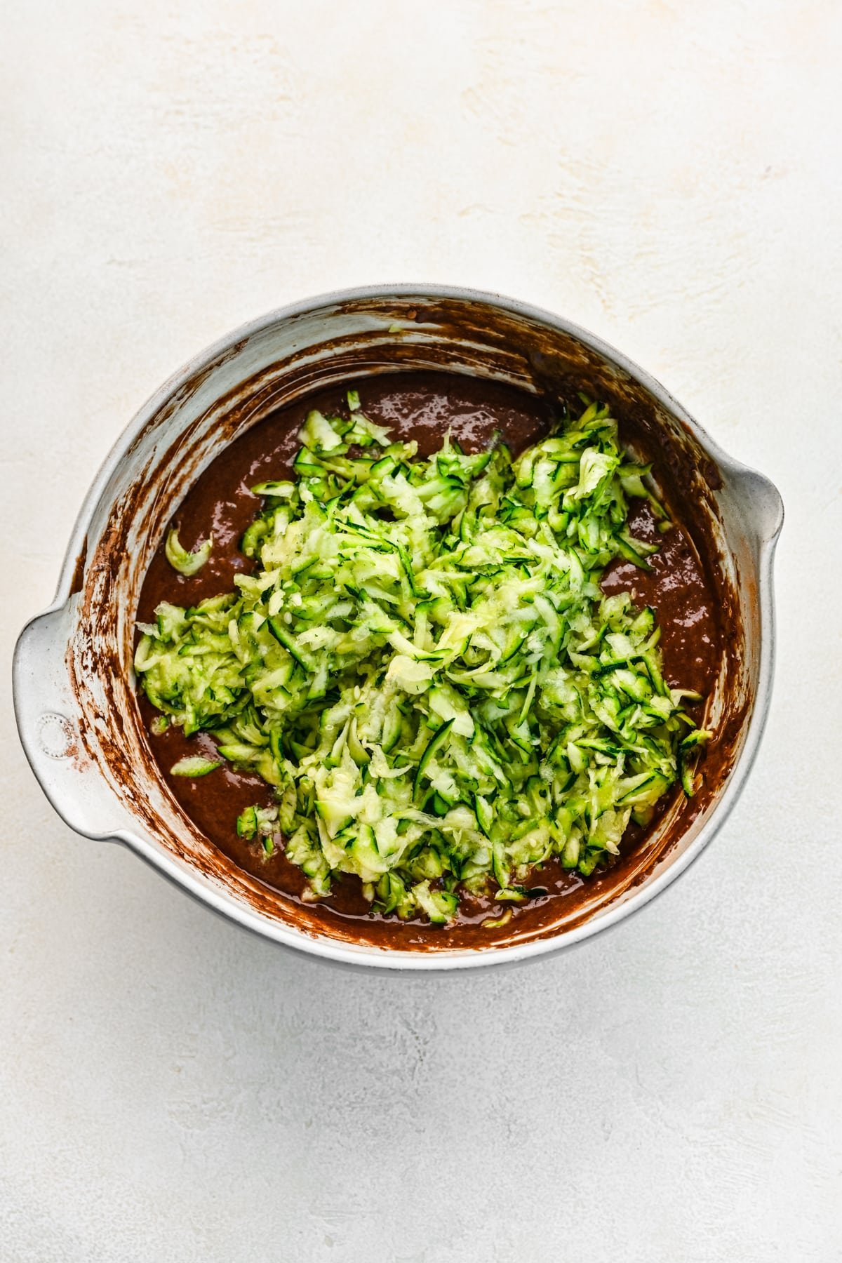 Grated zucchini on top of cake batter in a mixing bowl. 