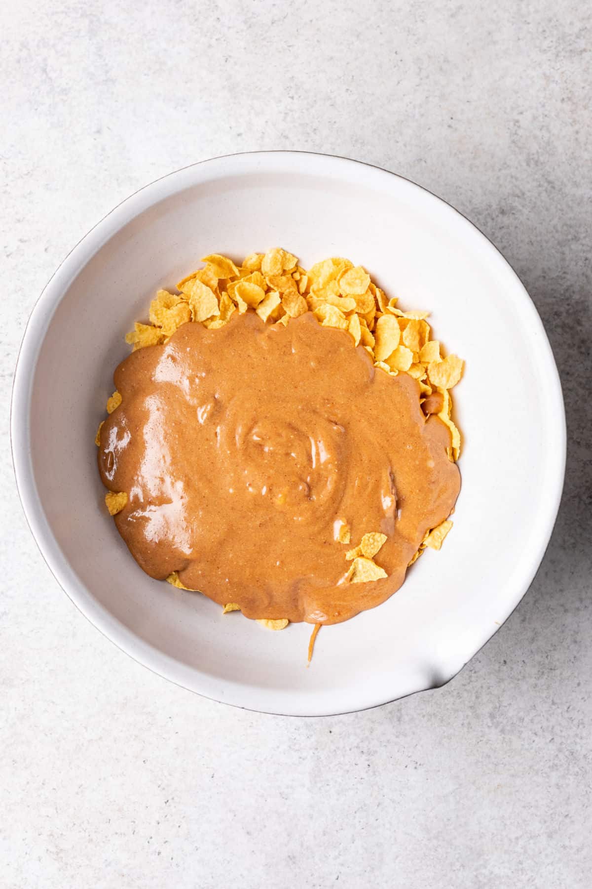 Peanut butter mixture on cornflakes in a mixing bowl. 