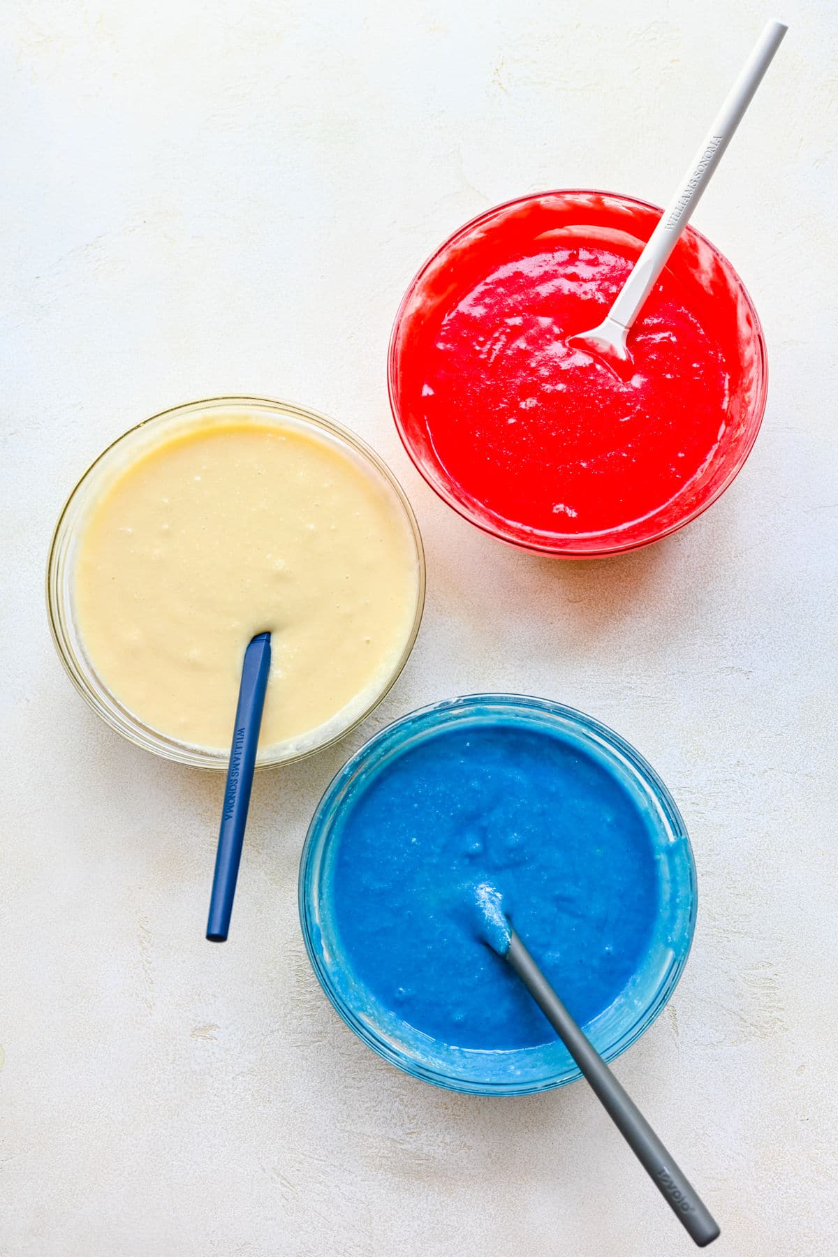 A dish of white batter, red batter, and blue batter in bowls. 
