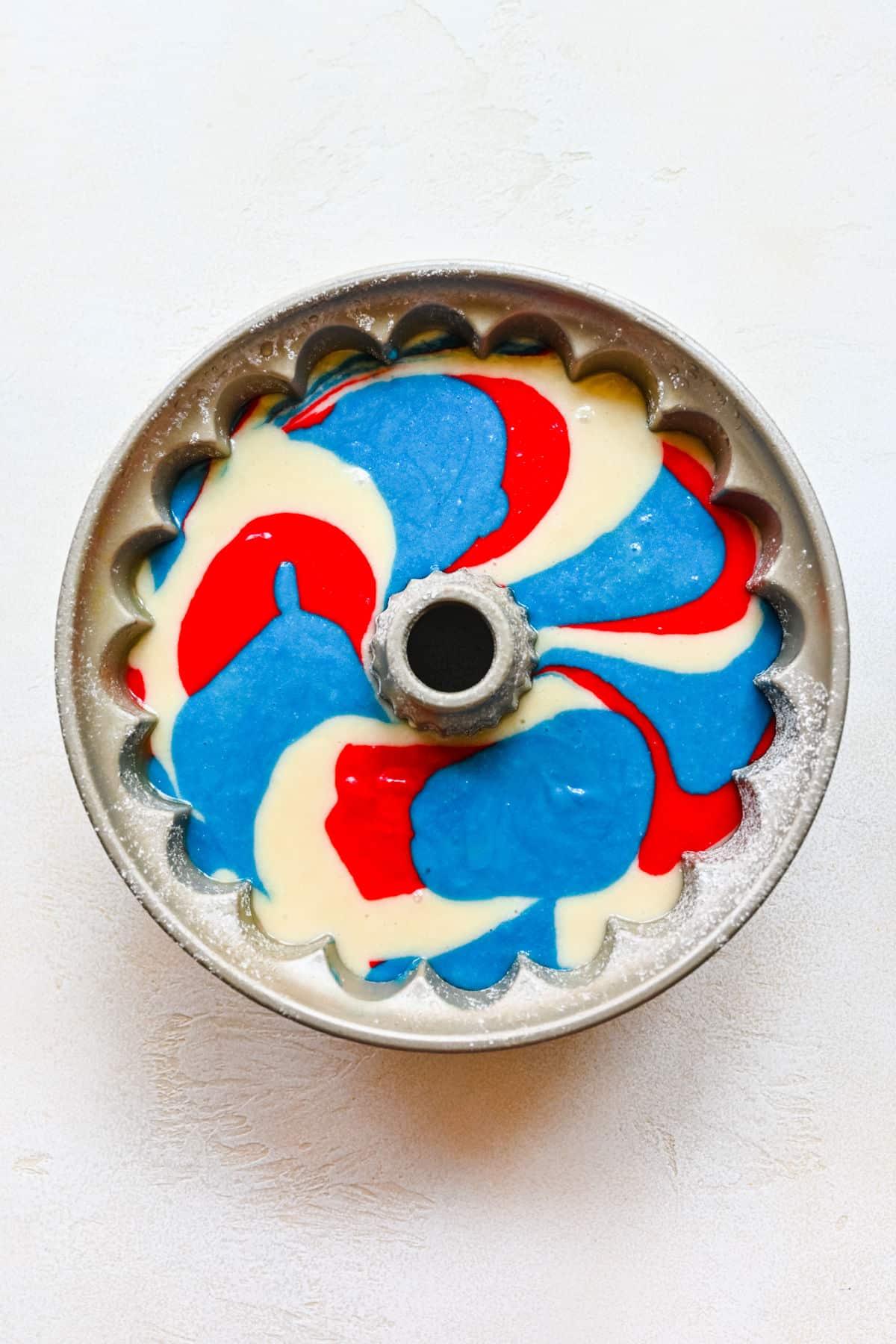 Red white and blue bundt cake batter in a bundt pan.