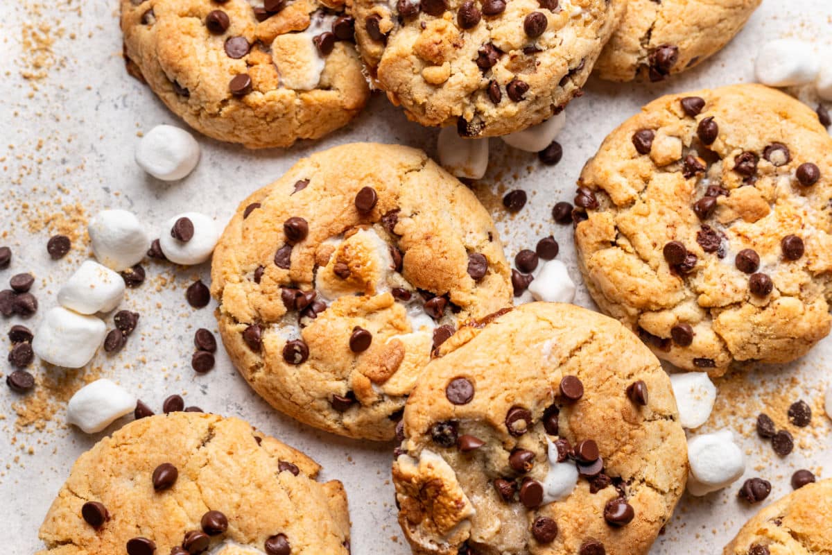 Overlapping s'mores cookies next to marshmallows and chocolate chips. 