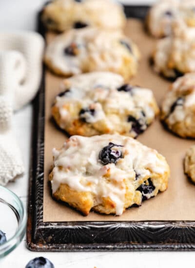 Rows of blueberry biscuits on brown parchment paper on a vintage baking sheet.