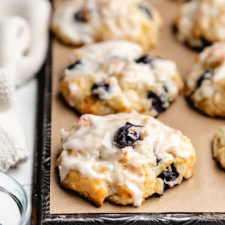 Rows of blueberry biscuits on brown parchment paper on a vintage baking sheet.