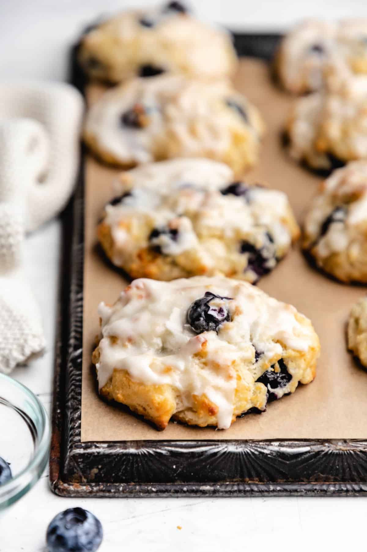 Rows of blueberry biscuits on brown parchment paper on a  vintage baking sheet. 