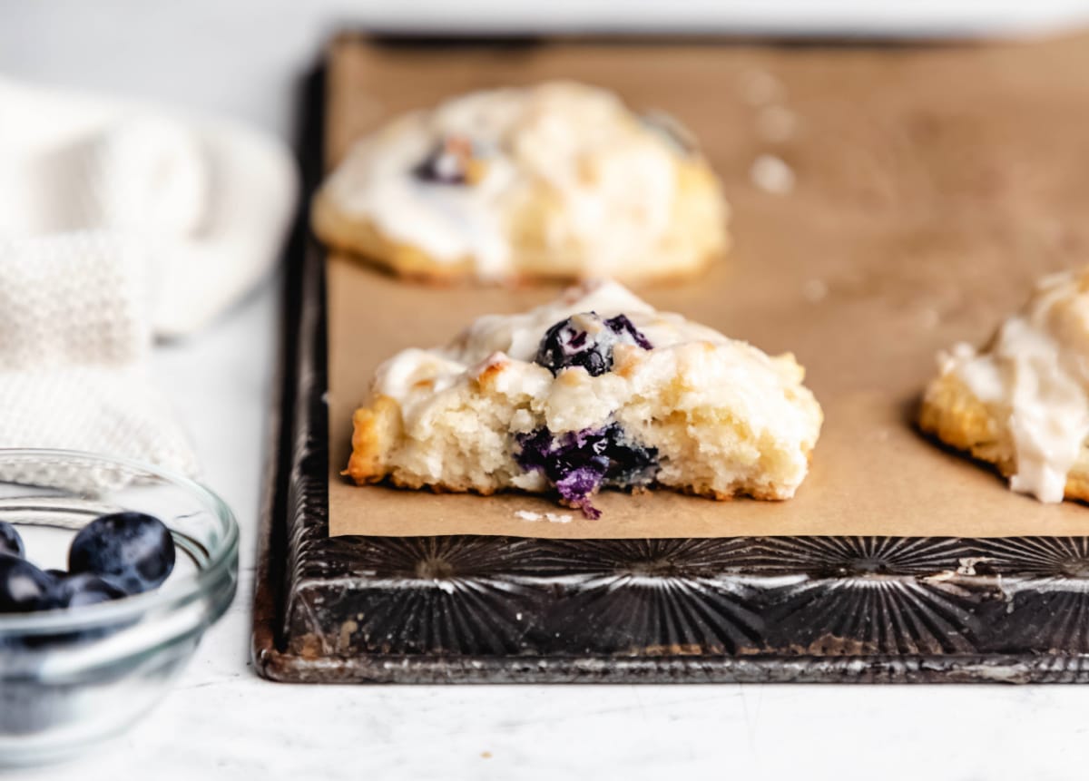 Half of a glazed blueberry biscuit next to a dish of blueberries. 