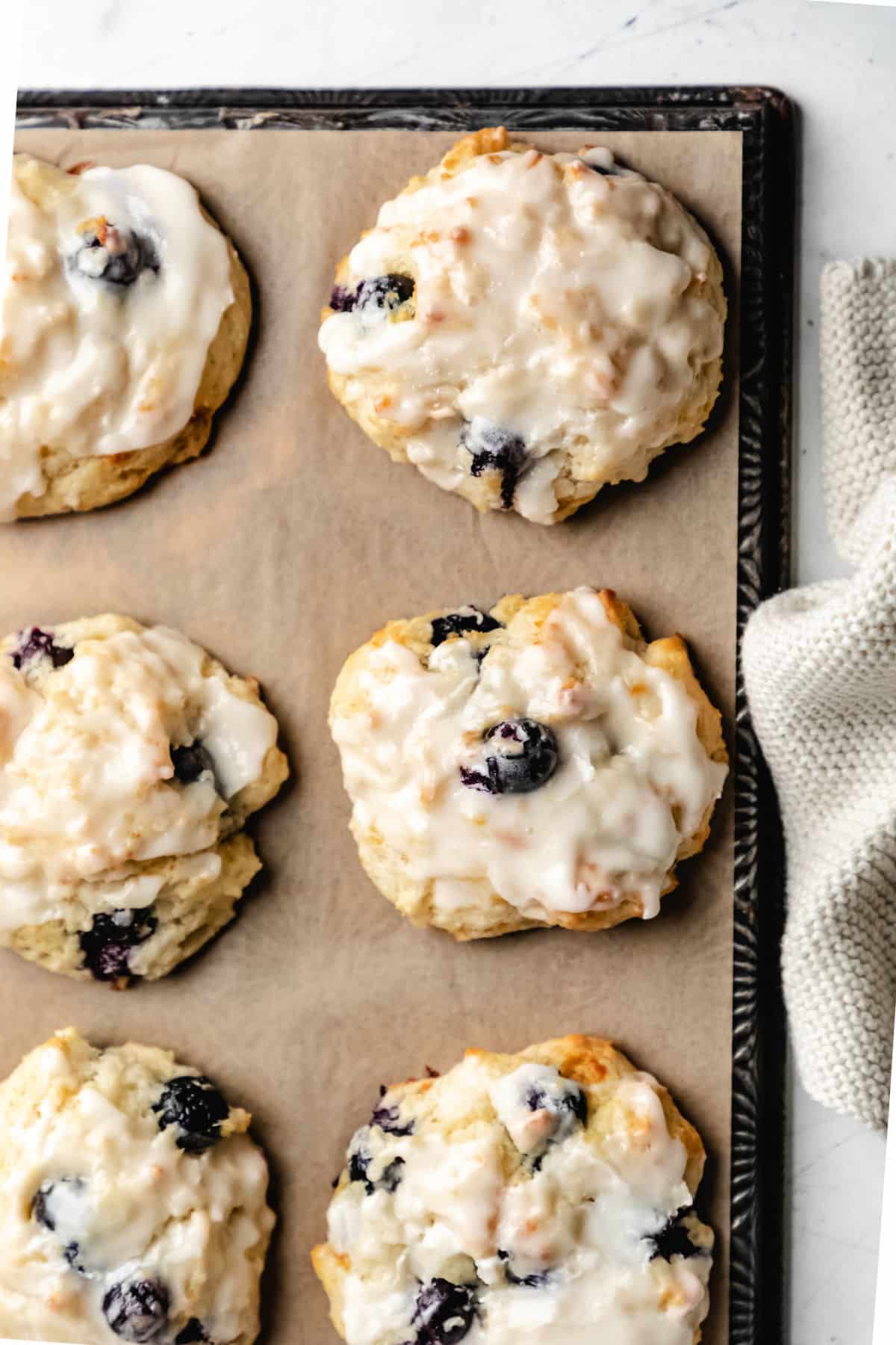 A tray of glazed blueberry biscuits next to a tan woven napkin.