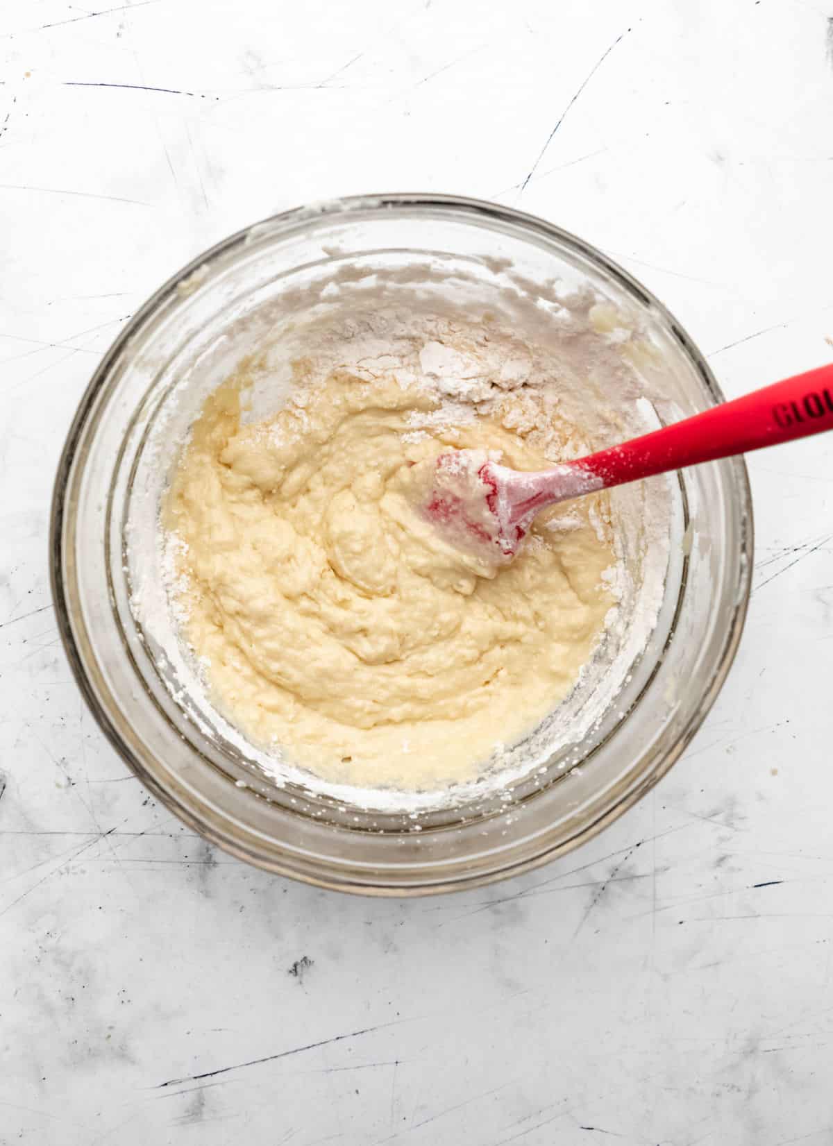 A red spatula stirring dry ingredients into the wet ingredients. 