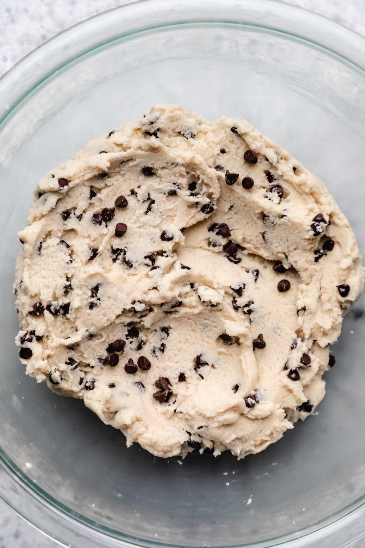Chocolate chips in raw cookie dough in a glass mixing bowl. 
