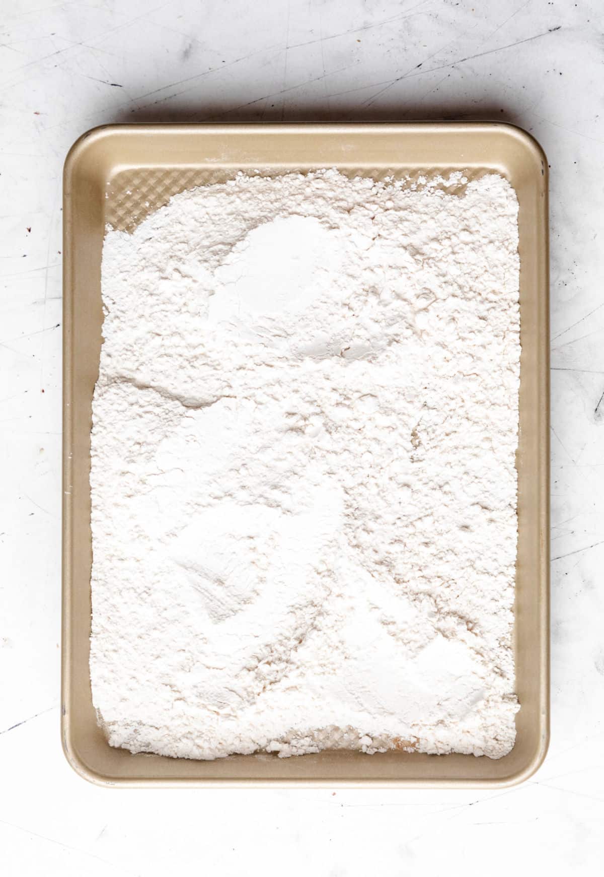 Flour spread out on rimmed baking sheet.