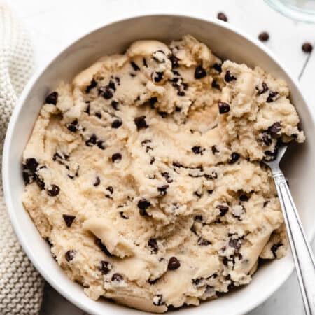 A bowl of edible cookie dough with a silver spoon holding a scoop.