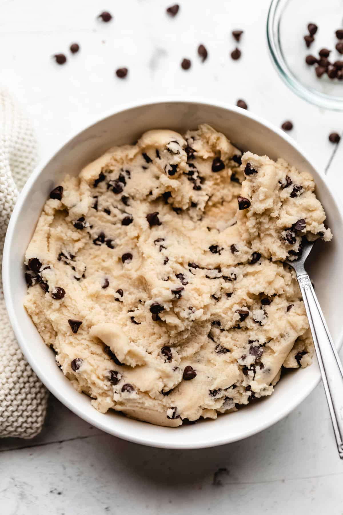 A bowl of edible cookie dough with a silver spoon holding a scoop. 