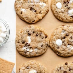 A row of s'mores cookies on brown parchment paper next to a dish of marshmallows.