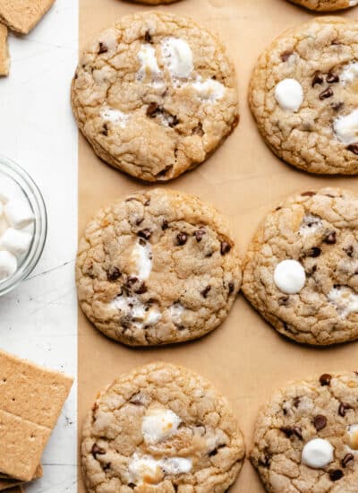 A row of s'mores cookies on brown parchment paper next to a dish of marshmallows.