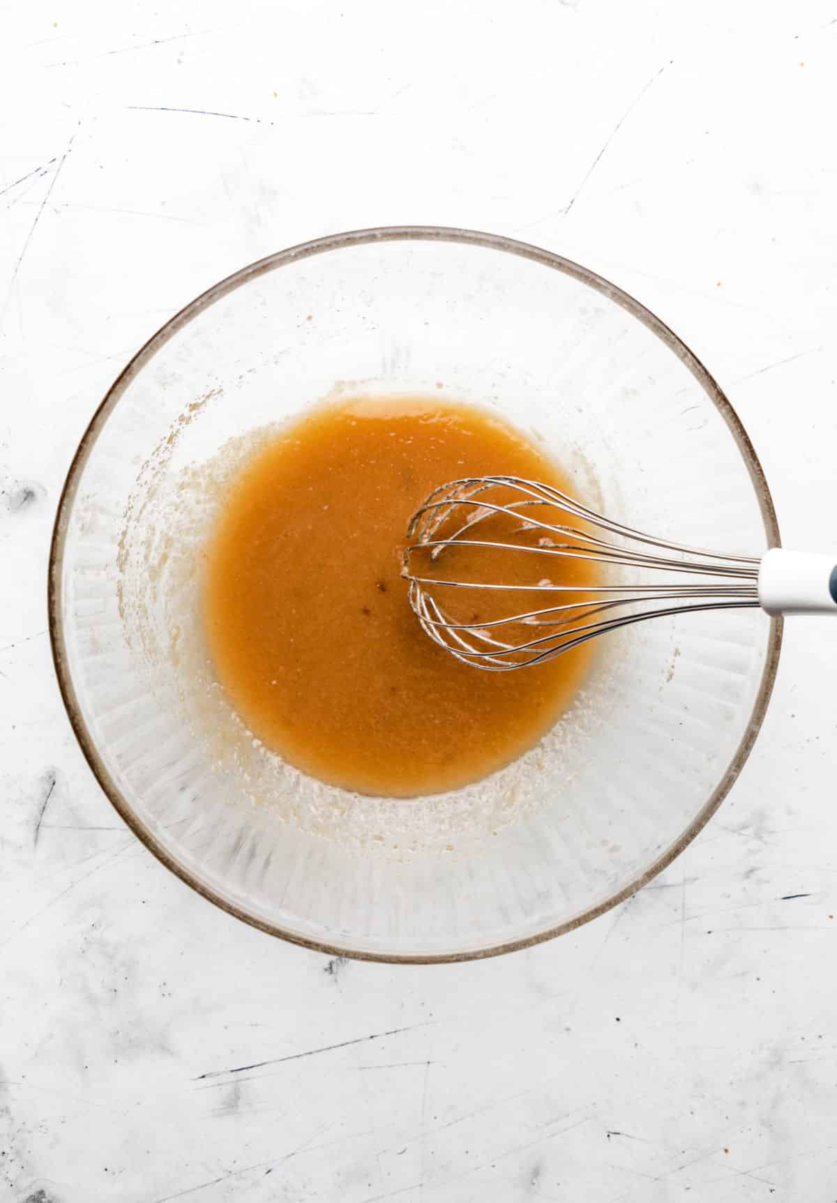 Melted butter and sugars whisked together in a glass mixing bowl. 