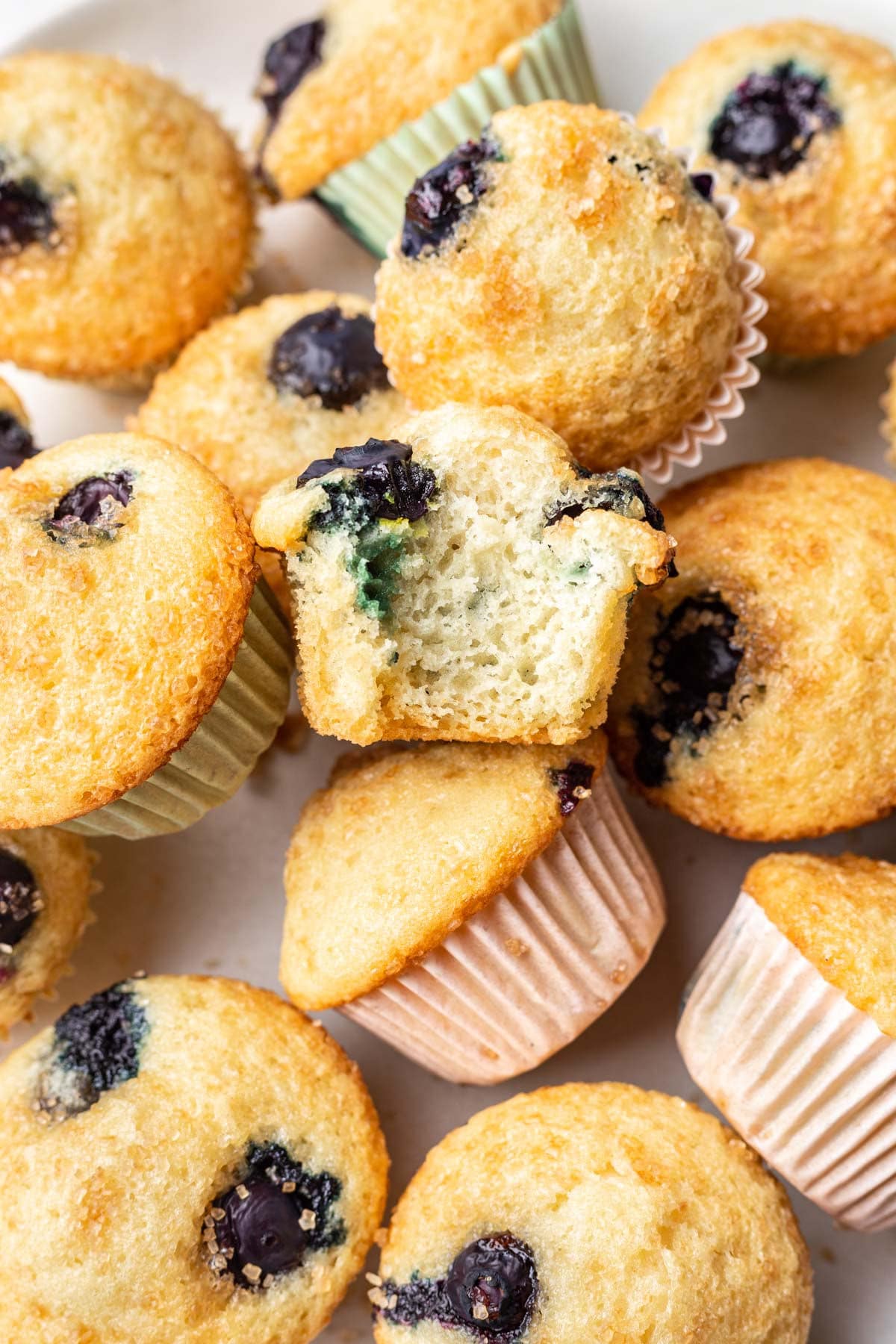 A plate of mini blueberry muffins with a bite missing from one muffin.
