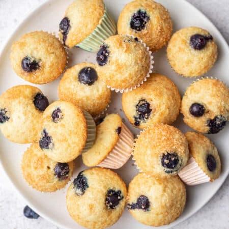 A plate of mini blueberry muffins next to a dish of blueberries.