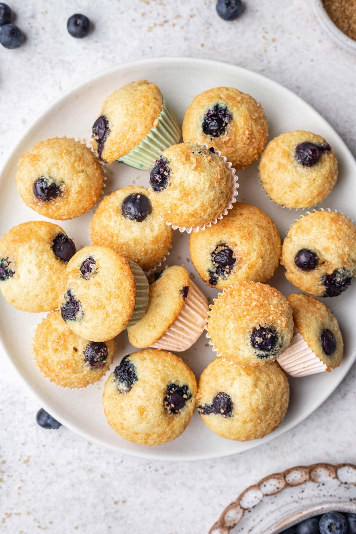A plate of mini blueberry muffins next to a dish of blueberries. 