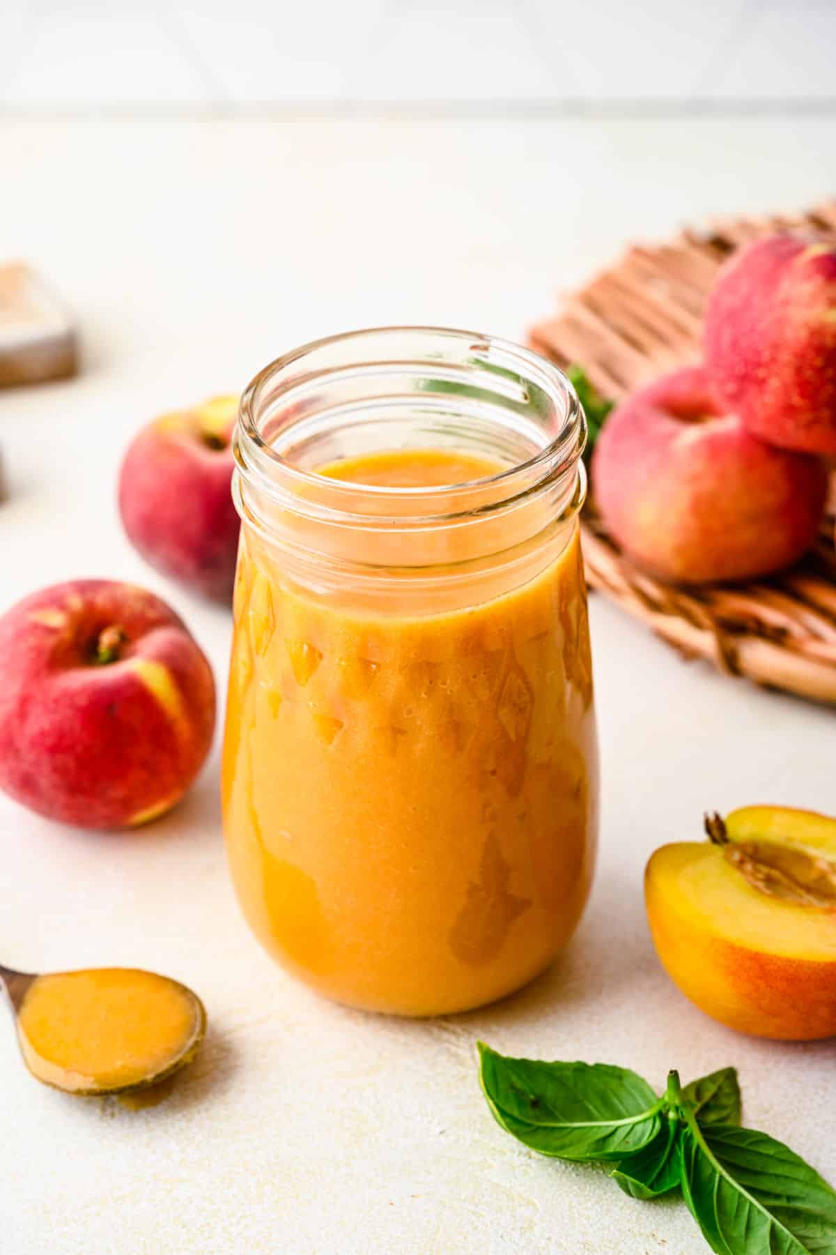 A glass jar filled with peach syrup next to fresh peaches. 