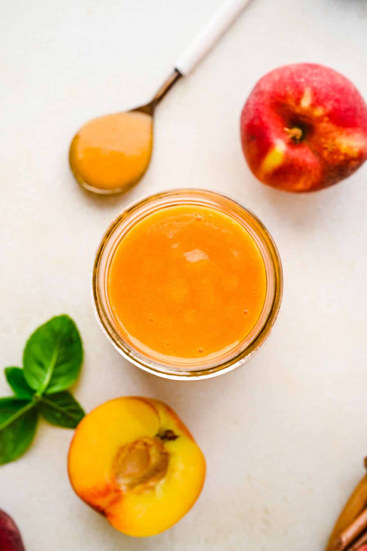 Overhead photo of peach syrup in a glass jar next to a spoon holding the syrup.