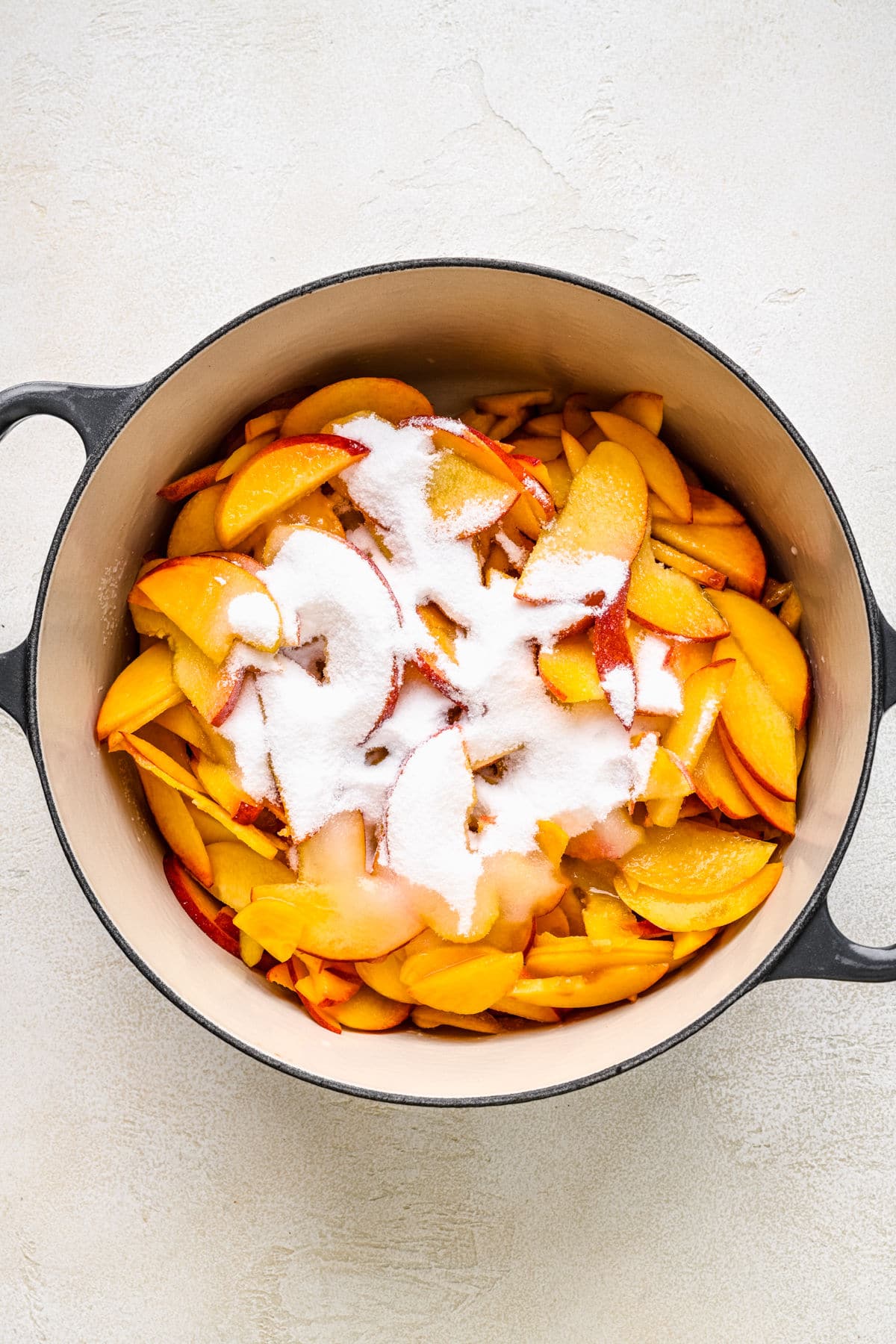 Peach slices topped with sugar in a Dutch oven.