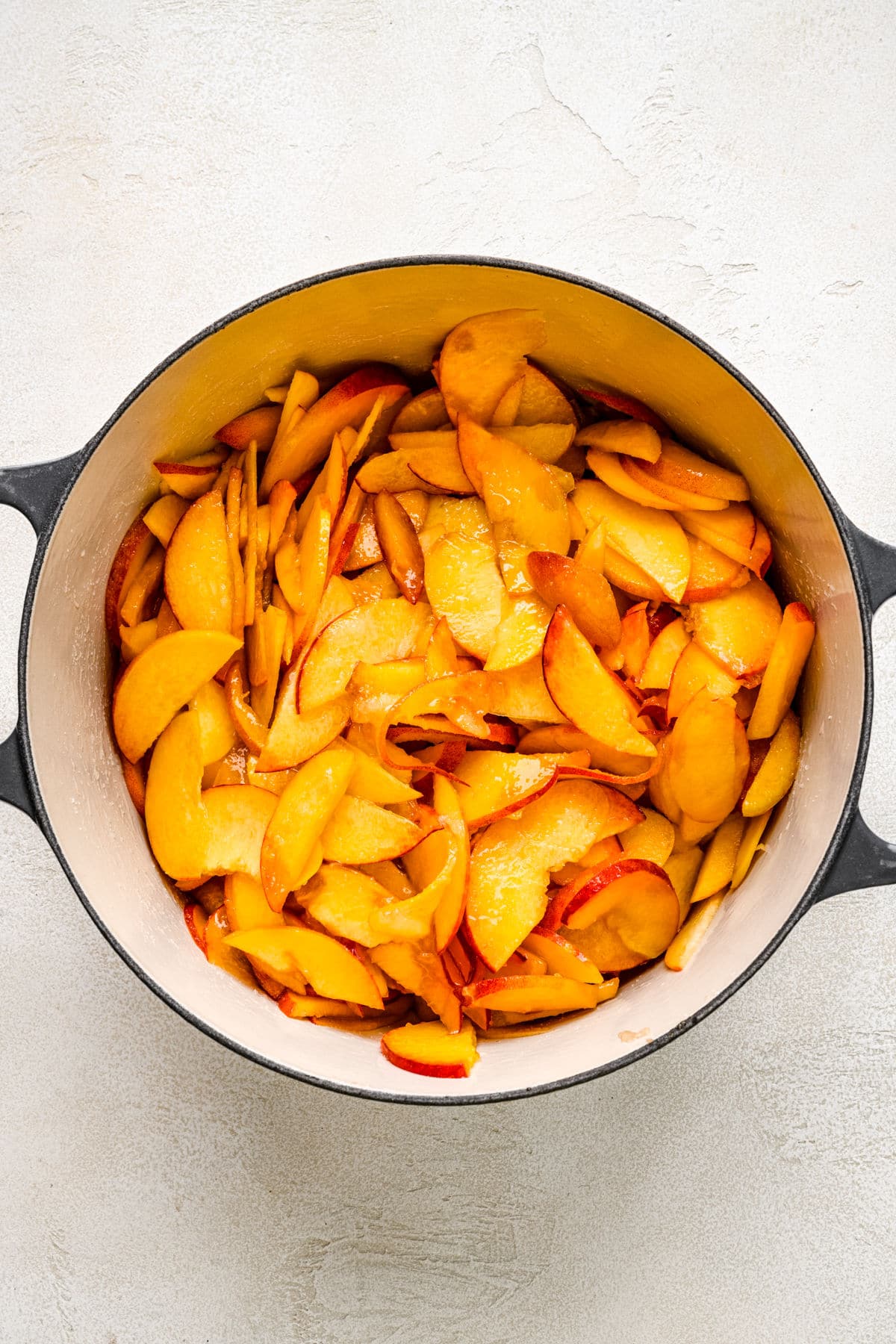 Peach slices with sugar lemon juice and water in a Dutch oven.