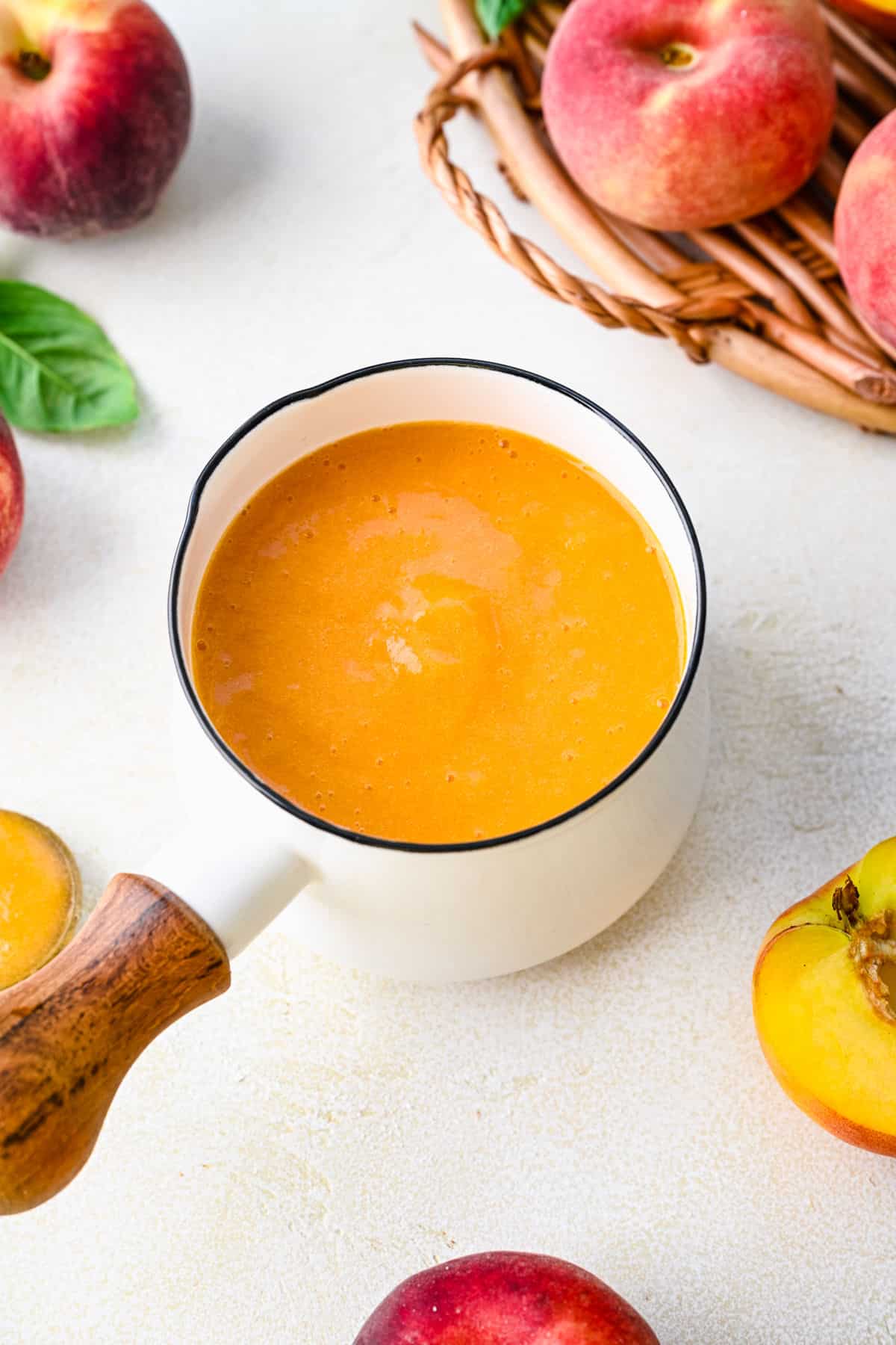 A small pot full of pureed peach syrup next to a halved peach.