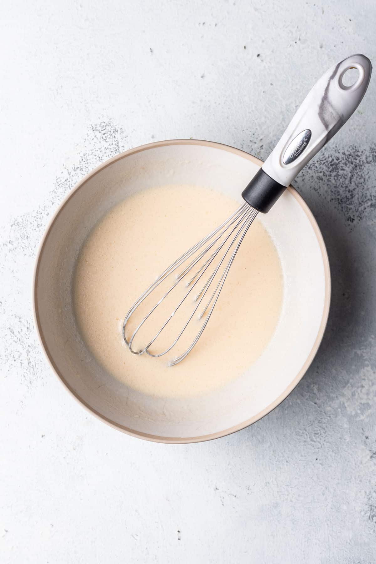 Wet ingredients for coconut muffins in a mixing bowl with a whisk in it.