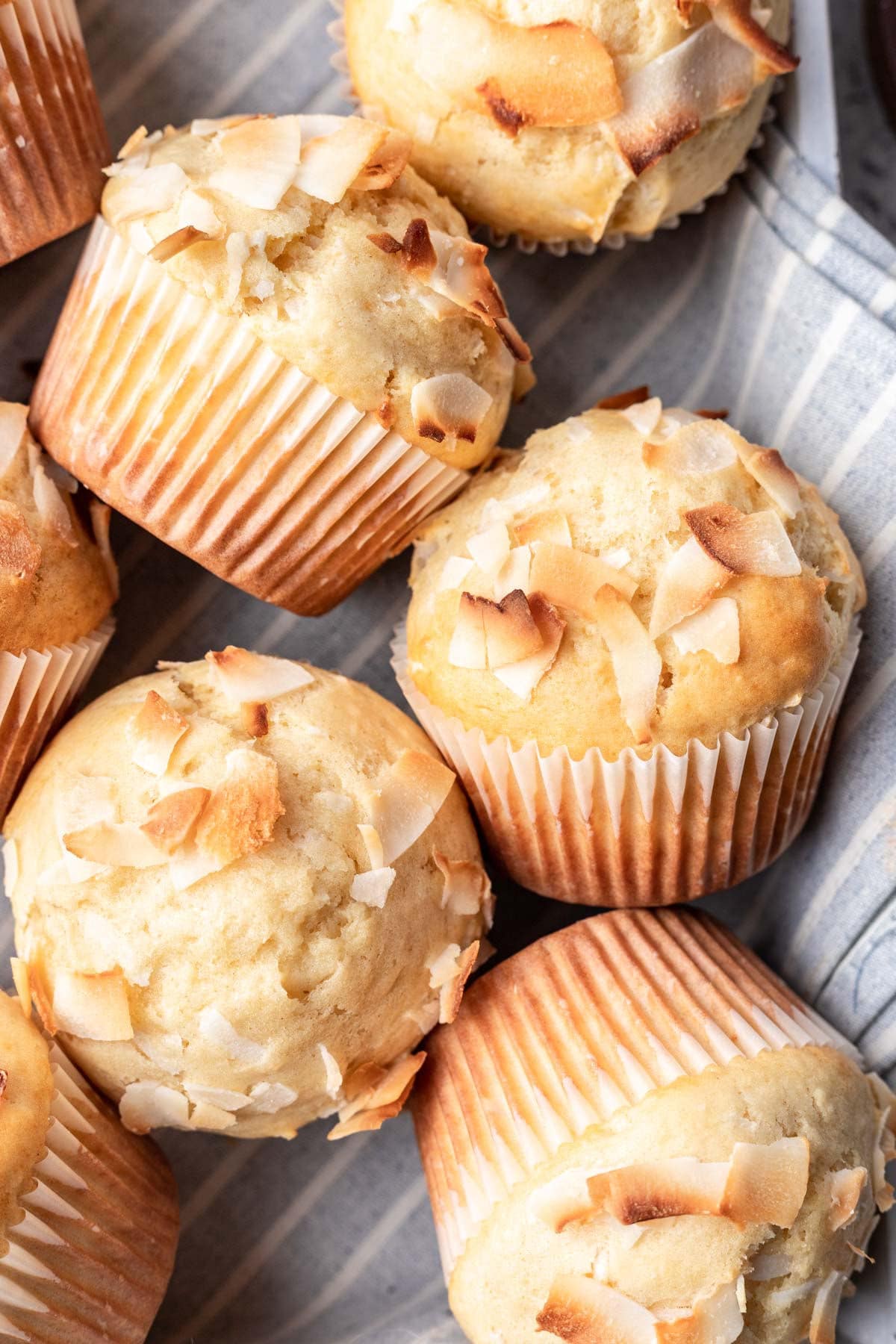 Four coconut muffins on their side on a striped dish towel. 