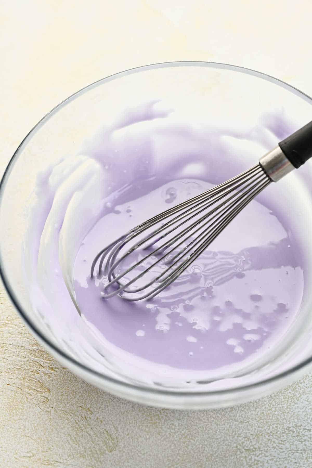 Lavender cookie glaze in a glass bowl with a whisk in it.
