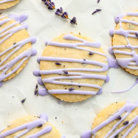 Iced lavender cookies on a piece of parchment paper next to a sprig of lavender.