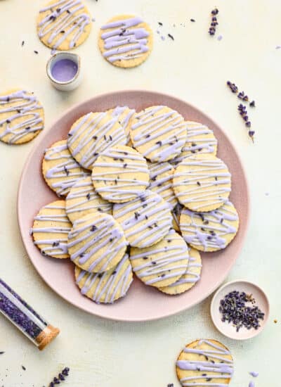 A plate of lavender cookies with a dish of lavender next to it.