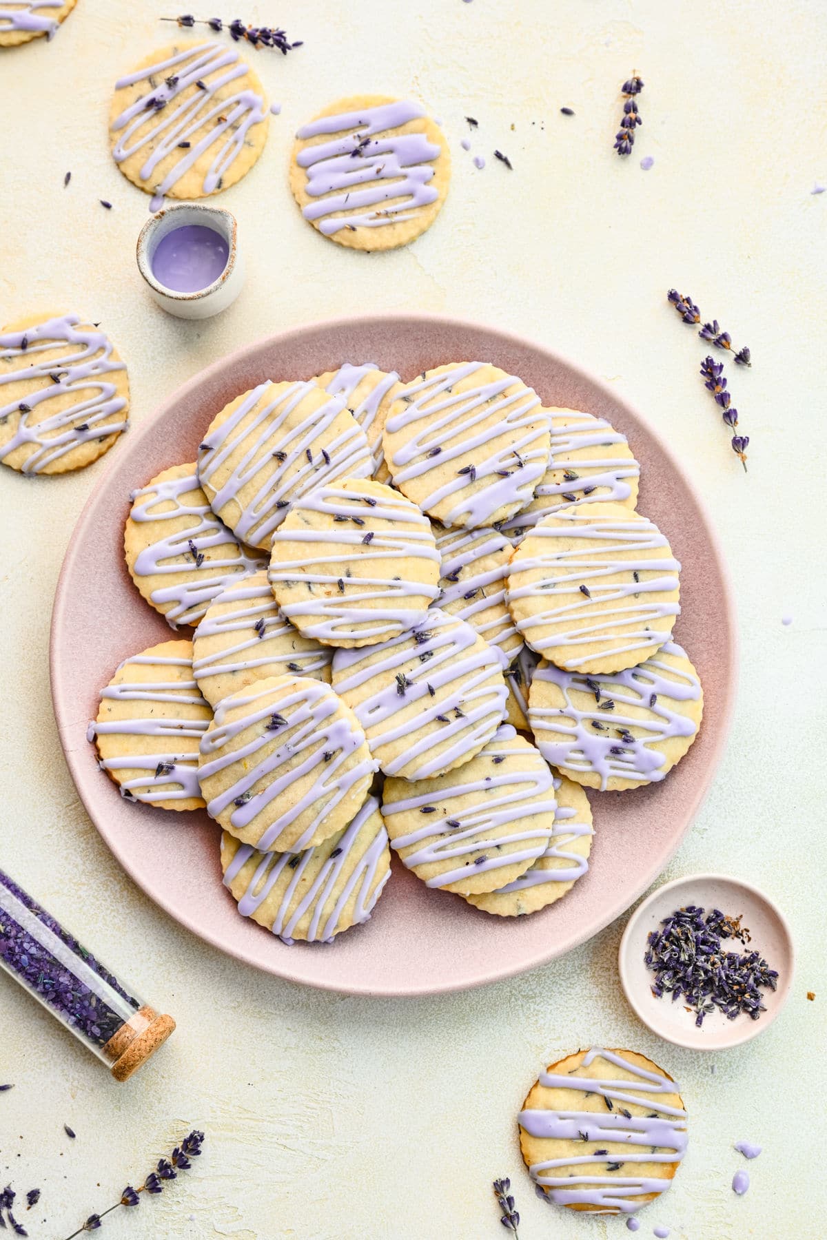 A plate of lavender cookies with lavender in a dish next to it.