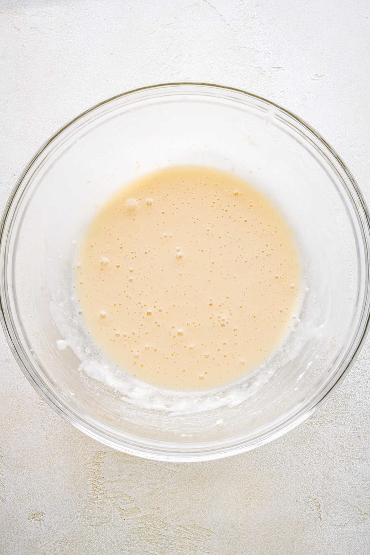 Wet ingredients for peach cake in a glass mixing bowl. 