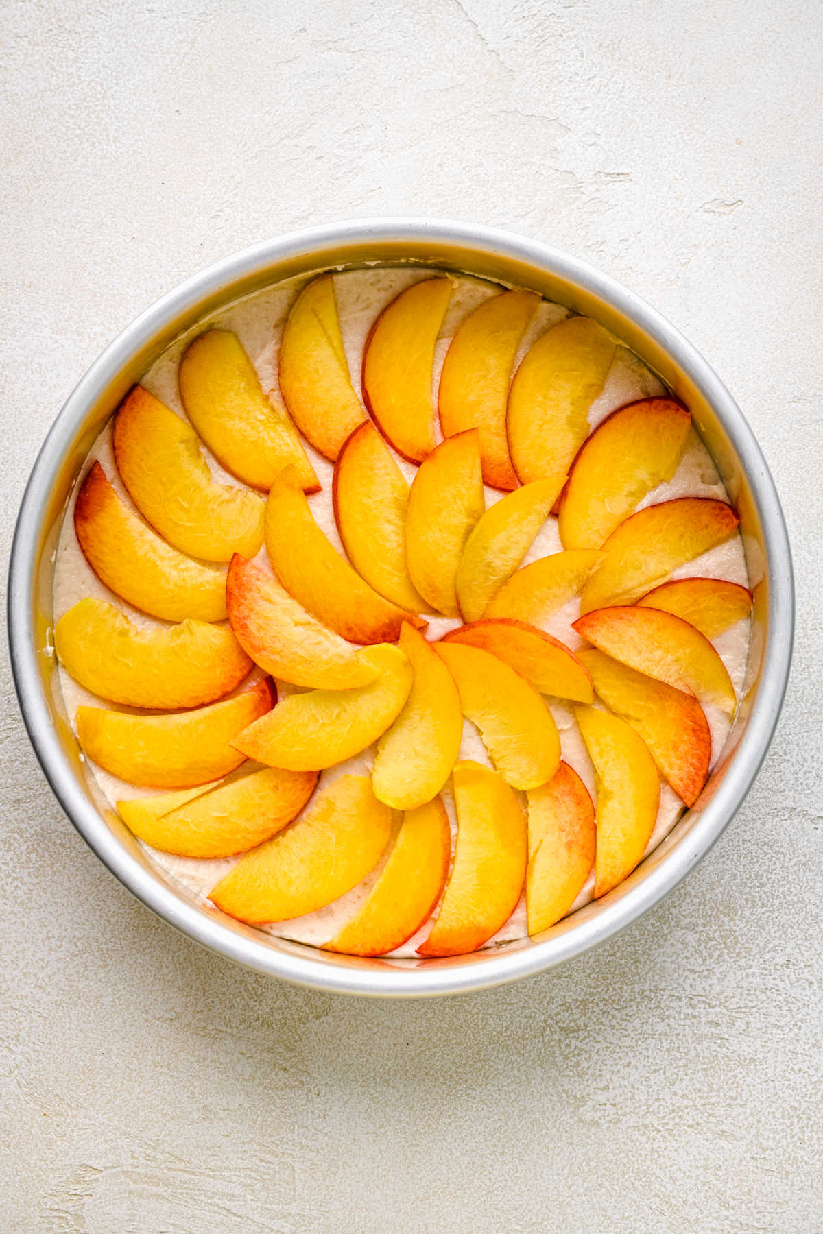 Slices of fresh peach over cake batter in a cake pan.
