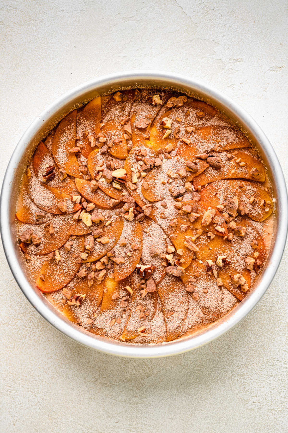 Cinnamon sugar and pecans over peach slices in a cake pan.