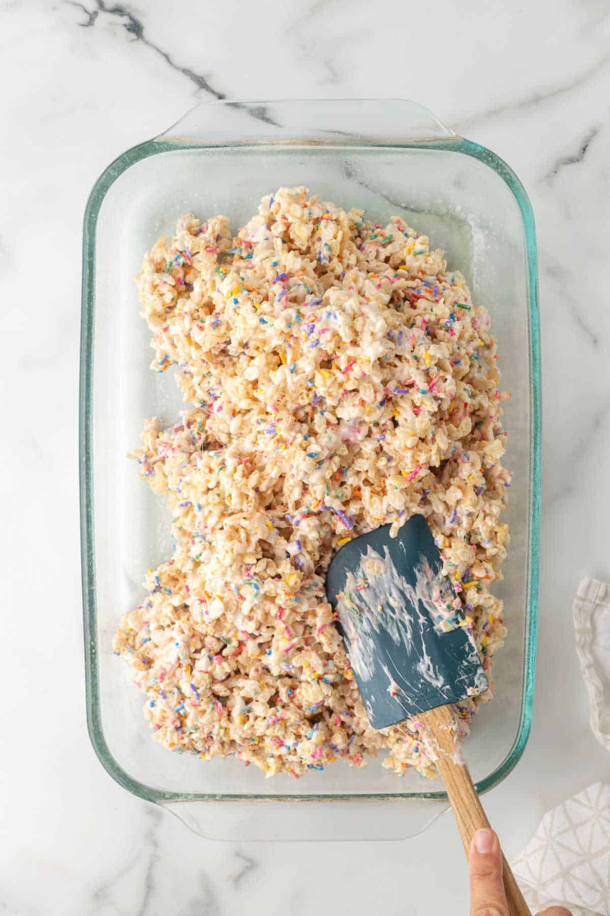 A spatula smoothing funfetti rice krispies treats into a glass pan.