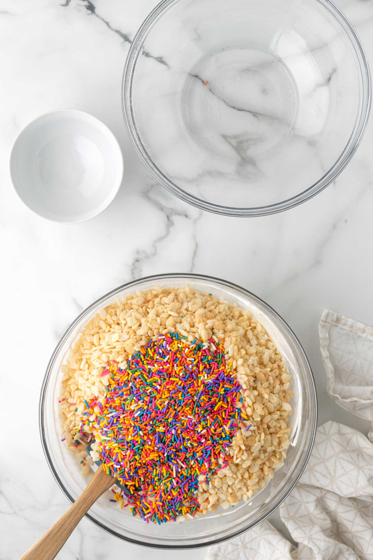 A spatula mixing rice krispies cereal and sprinkles into melted marshmallow.