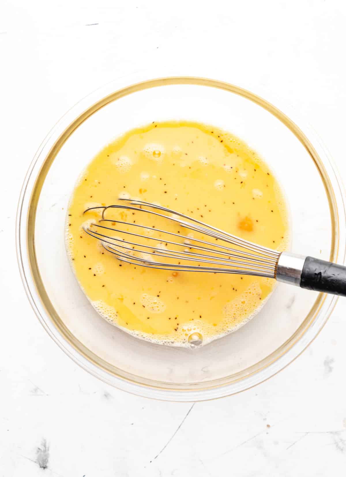 Whisked eggs and pepper in a glass mixing bowl. 