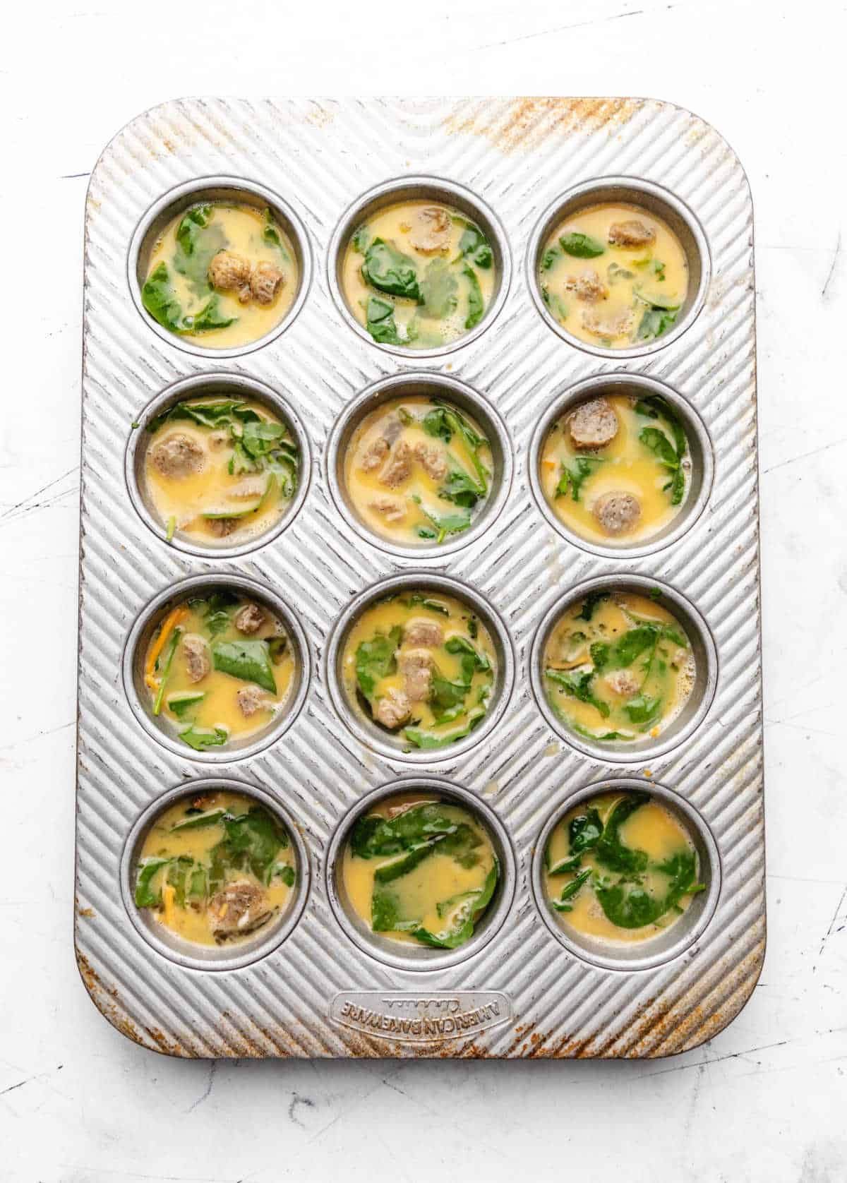 Raw egg spinach and sausage in a muffin tin.