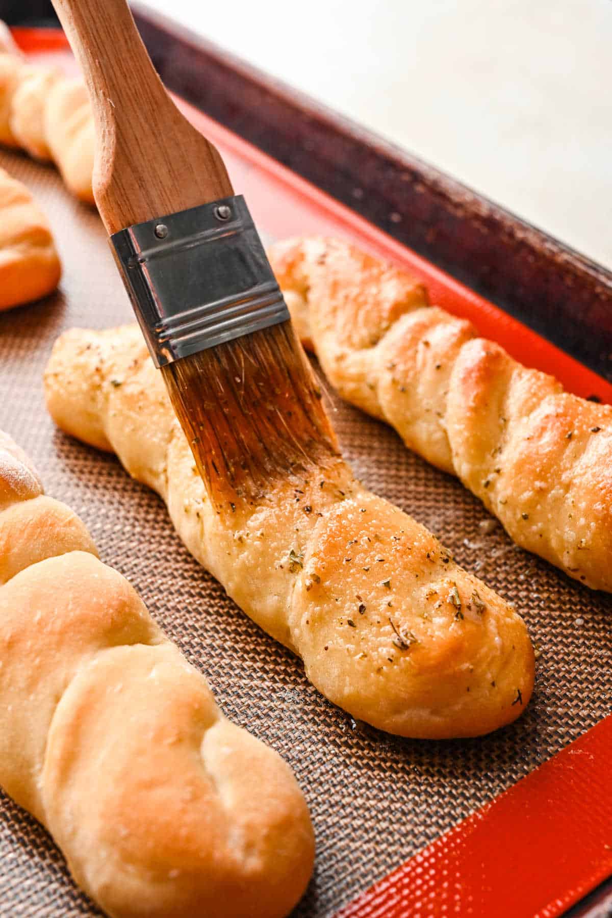 A basting brush brushing garlic butter onto baked breadsticks.