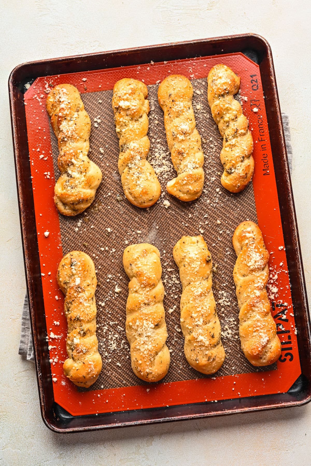 Homemade breadsticks on a baking pan on top of a kitchen towel.